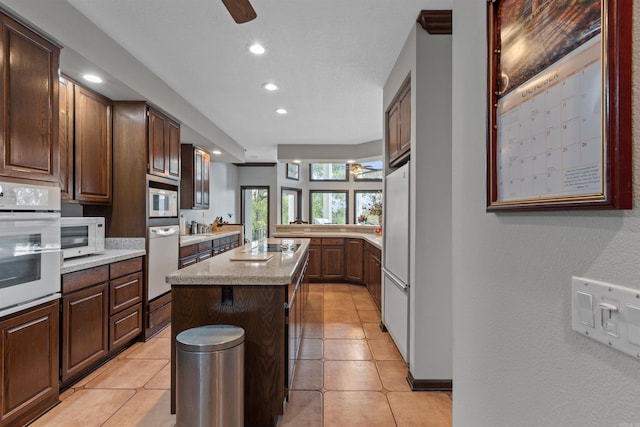 kitchen with light tile patterned flooring, a center island, dark brown cabinets, and white appliances