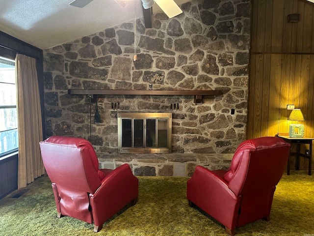 living room with a stone fireplace, wooden walls, vaulted ceiling, and dark colored carpet