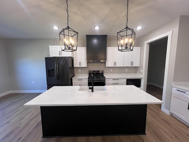 kitchen featuring black refrigerator with ice dispenser, wall chimney range hood, a kitchen island with sink, and hanging light fixtures