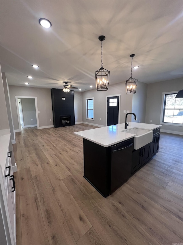 kitchen with an island with sink, dishwasher, hanging light fixtures, light hardwood / wood-style flooring, and sink