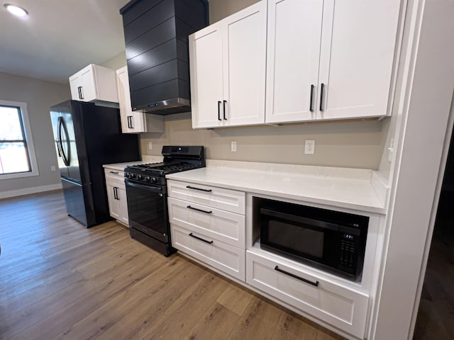 kitchen with premium range hood, white cabinetry, light hardwood / wood-style flooring, and black appliances