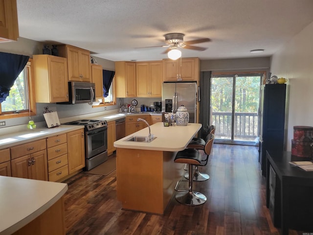 kitchen featuring a center island with sink, sink, appliances with stainless steel finishes, a kitchen bar, and dark wood-type flooring