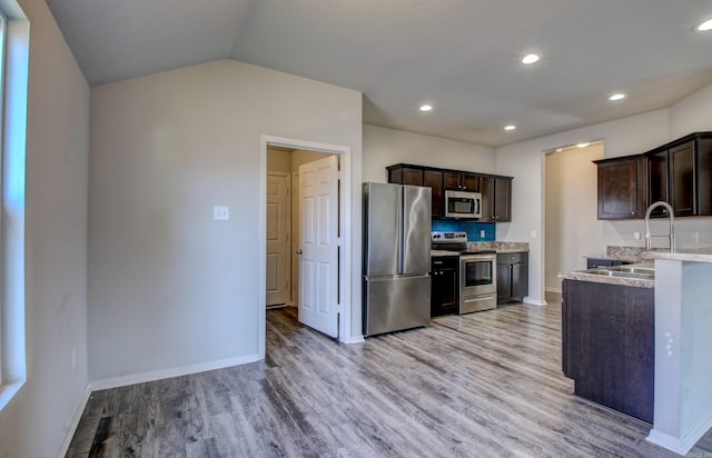 kitchen featuring light hardwood / wood-style flooring, stainless steel appliances, light stone countertops, vaulted ceiling, and dark brown cabinetry