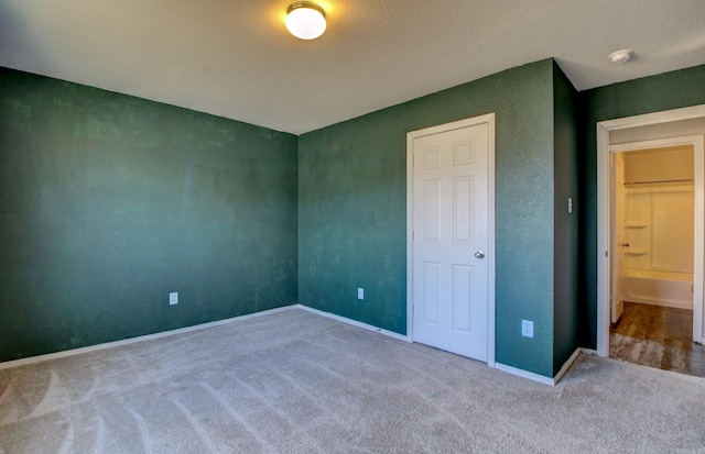 unfurnished bedroom with ensuite bath, a textured ceiling, and carpet floors