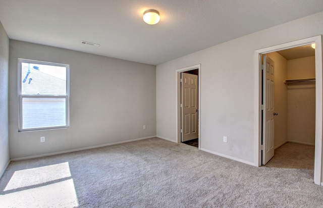 unfurnished bedroom featuring a closet, light colored carpet, and a walk in closet