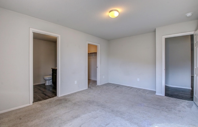 unfurnished bedroom featuring a closet, a spacious closet, light colored carpet, and connected bathroom