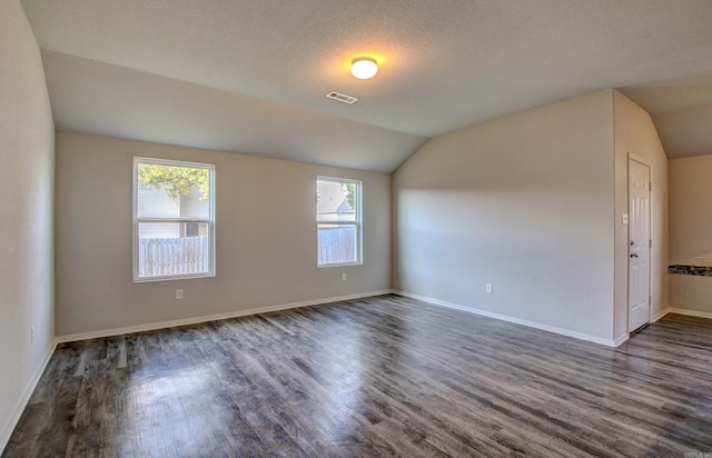 spare room featuring a textured ceiling, vaulted ceiling, and dark hardwood / wood-style floors