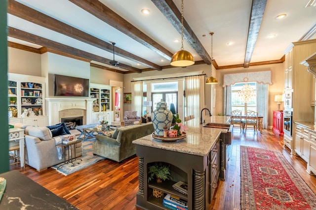 kitchen featuring stainless steel oven, beamed ceiling, a center island with sink, decorative light fixtures, and dark hardwood / wood-style flooring