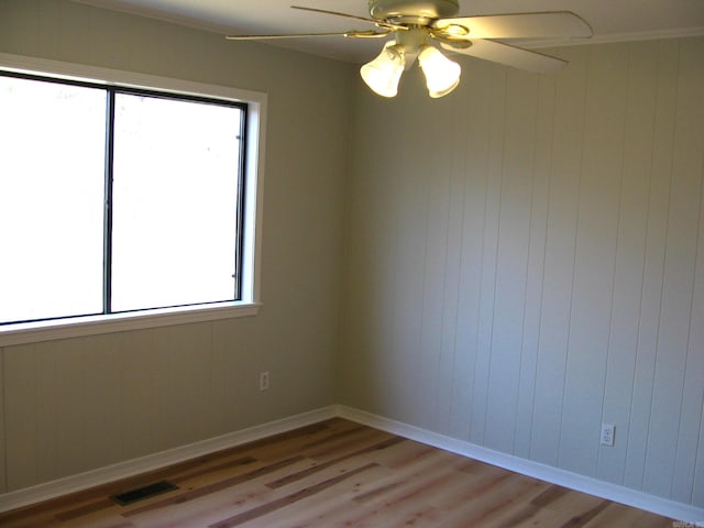 empty room featuring ornamental molding, wood walls, wood-type flooring, and ceiling fan