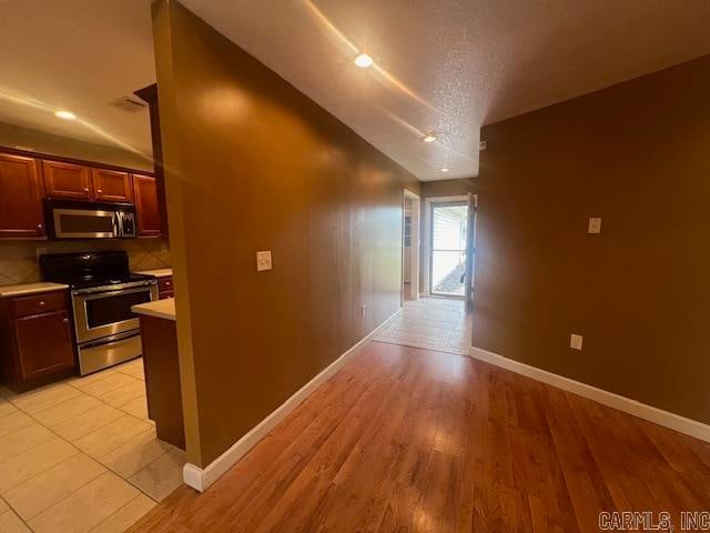 hallway with a textured ceiling, lofted ceiling, and light wood-type flooring