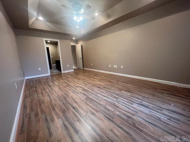 unfurnished bedroom with a tray ceiling and dark wood-type flooring