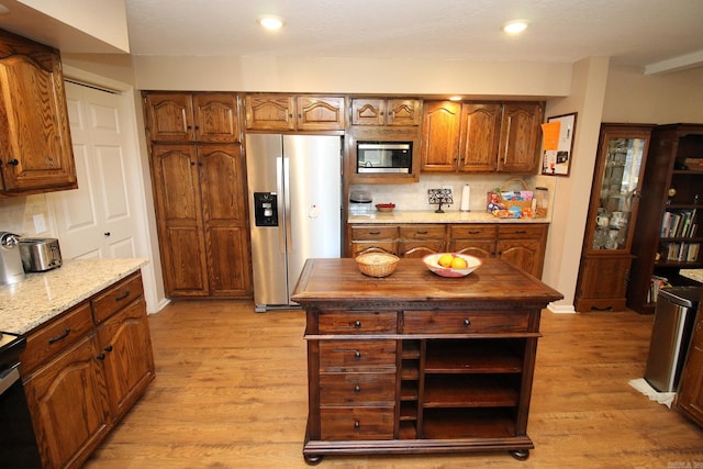 kitchen with appliances with stainless steel finishes, light hardwood / wood-style flooring, tasteful backsplash, and light stone counters