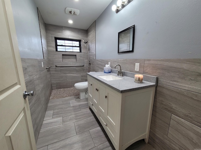 bathroom with vanity, toilet, tile walls, and a tile shower