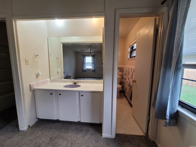 bathroom with toilet, a healthy amount of sunlight, vanity, and ceiling fan