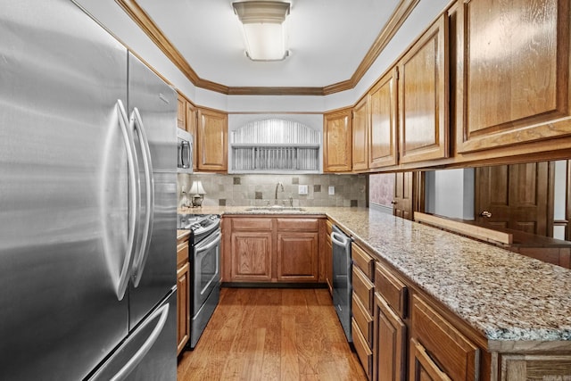 kitchen with light stone countertops, appliances with stainless steel finishes, sink, light wood-type flooring, and crown molding