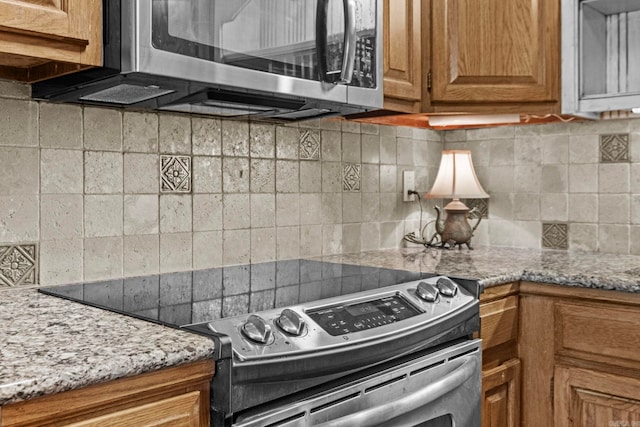 kitchen with appliances with stainless steel finishes, light stone countertops, and backsplash