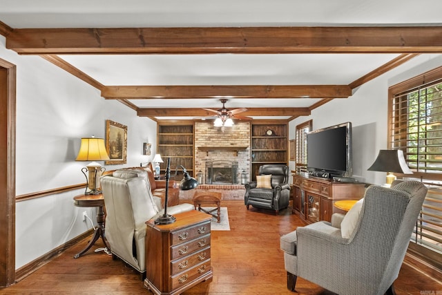 living room featuring beamed ceiling, hardwood / wood-style floors, a brick fireplace, built in shelves, and ceiling fan