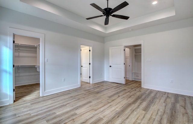 unfurnished bedroom with a closet, a walk in closet, a tray ceiling, light hardwood / wood-style floors, and ceiling fan