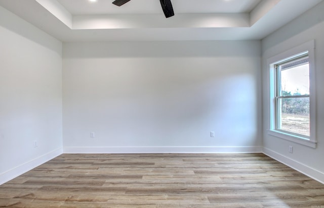 empty room with a raised ceiling, light wood-type flooring, and ceiling fan