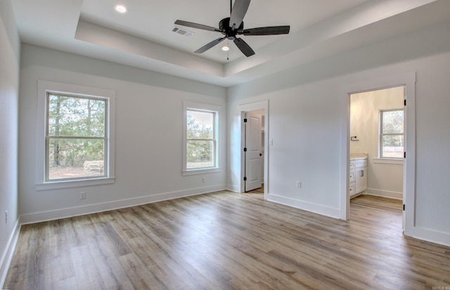 unfurnished bedroom featuring connected bathroom, ceiling fan, a raised ceiling, and multiple windows