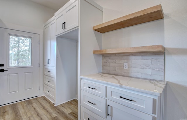 kitchen featuring light stone countertops, light wood-type flooring, white cabinetry, and tasteful backsplash