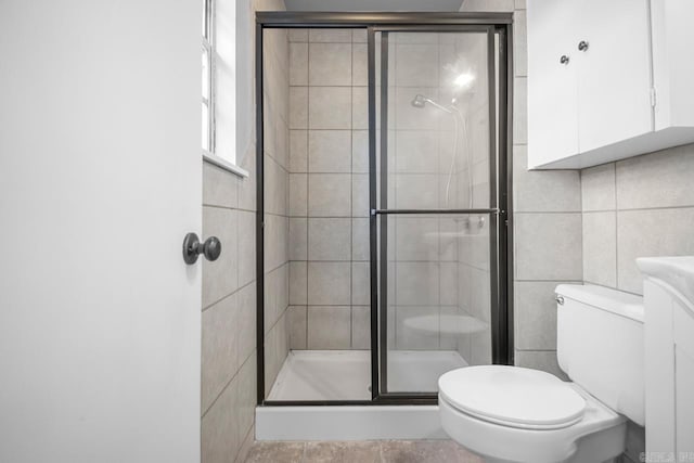 bathroom featuring tile walls, toilet, a shower with shower door, vanity, and tile patterned flooring