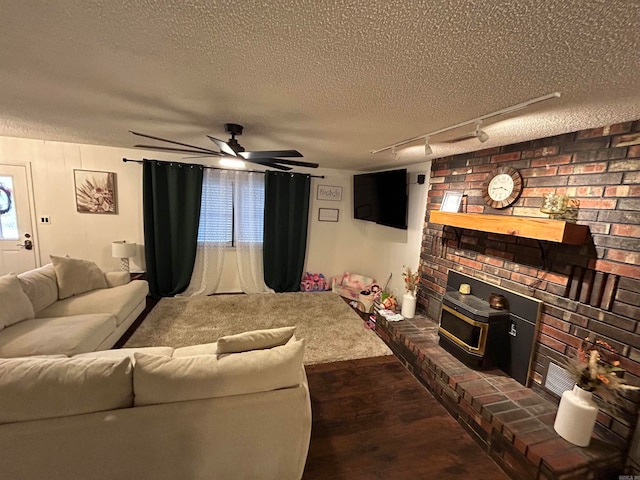 living room with a textured ceiling, a wood stove, ceiling fan, dark wood-type flooring, and track lighting