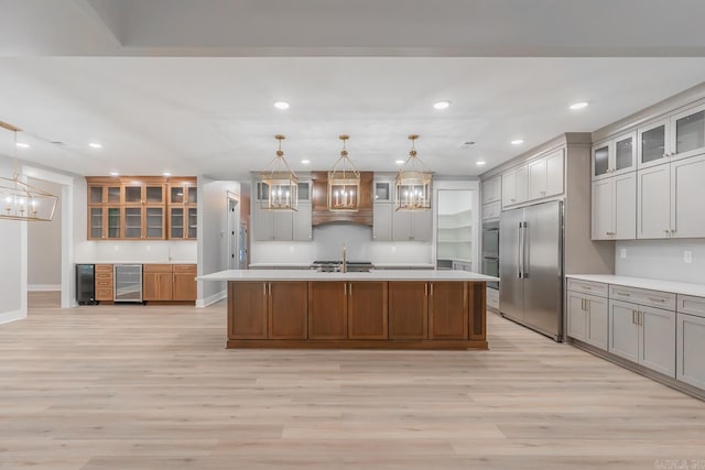 kitchen with stainless steel built in refrigerator, light wood-type flooring, decorative light fixtures, and an island with sink