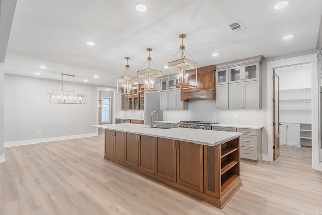 kitchen with stainless steel gas cooktop, hanging light fixtures, sink, a spacious island, and light hardwood / wood-style flooring