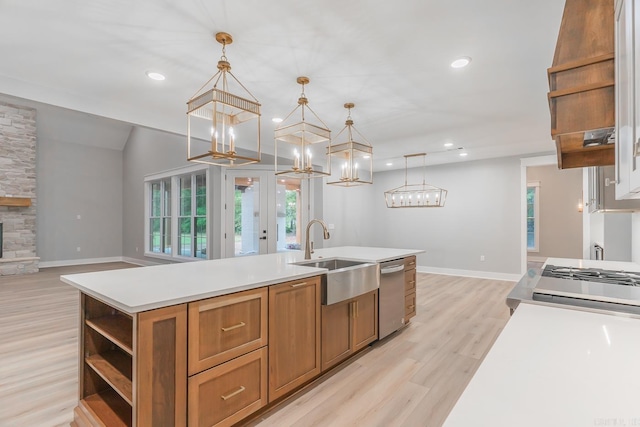 kitchen with a center island with sink, dishwasher, hanging light fixtures, sink, and light wood-type flooring