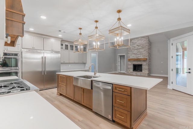 kitchen featuring stainless steel appliances, a center island with sink, white cabinetry, decorative light fixtures, and light hardwood / wood-style flooring