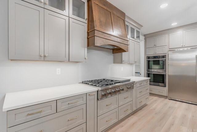 kitchen featuring gray cabinets, custom exhaust hood, light hardwood / wood-style floors, and stainless steel appliances