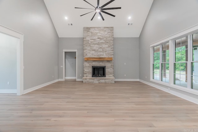 unfurnished living room featuring a stone fireplace, high vaulted ceiling, light hardwood / wood-style floors, and ceiling fan