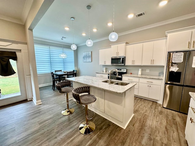 kitchen with pendant lighting, white cabinets, a center island with sink, and stainless steel appliances