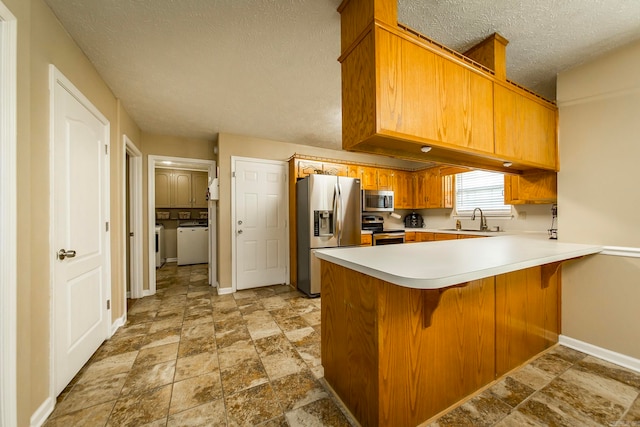 kitchen with independent washer and dryer, kitchen peninsula, sink, appliances with stainless steel finishes, and a textured ceiling