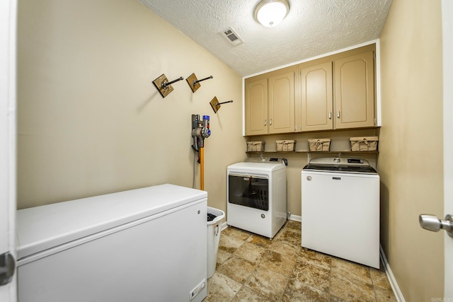 laundry area with cabinets, a textured ceiling, and washing machine and clothes dryer