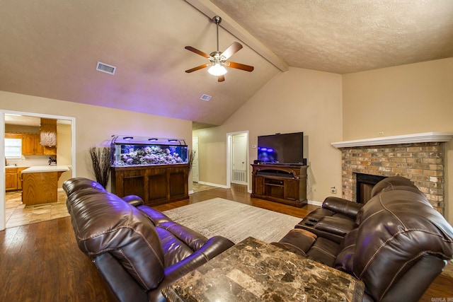 living room featuring ceiling fan, a textured ceiling, wood-type flooring, vaulted ceiling with beams, and a fireplace