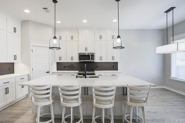 kitchen with appliances with stainless steel finishes, a center island with sink, light wood-type flooring, and pendant lighting