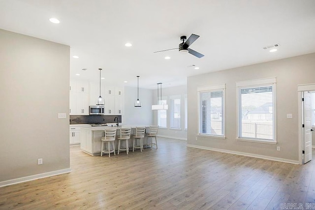 kitchen featuring an island with sink, a kitchen bar, pendant lighting, light wood-type flooring, and white cabinets