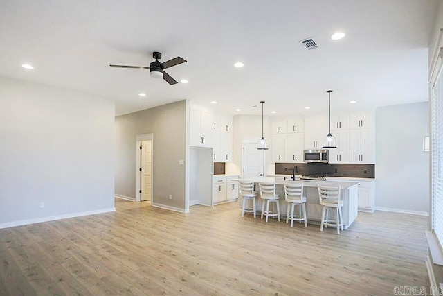 kitchen featuring light hardwood / wood-style floors, white cabinetry, a kitchen island with sink, and decorative light fixtures