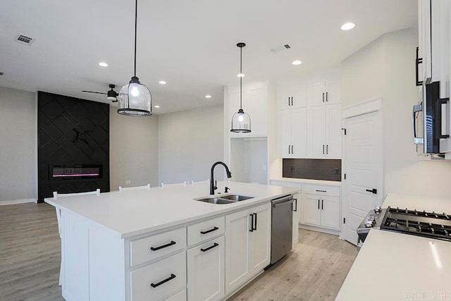 kitchen with appliances with stainless steel finishes, sink, hanging light fixtures, and an island with sink