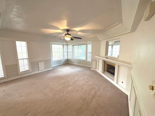 unfurnished living room with ceiling fan, a textured ceiling, a tray ceiling, and carpet flooring