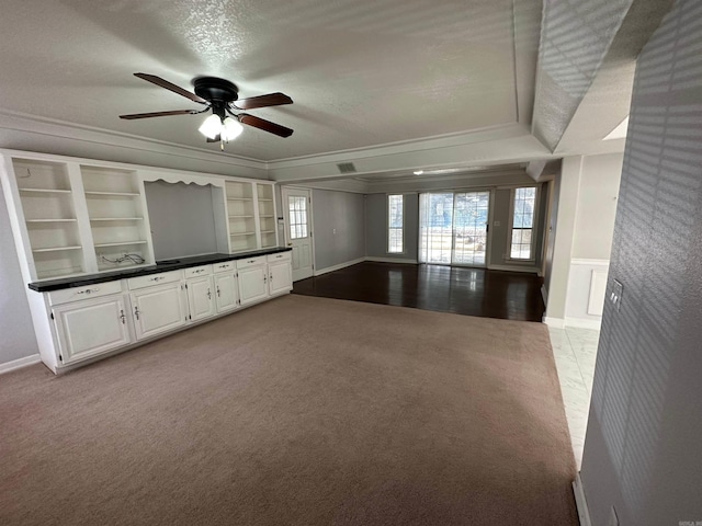 unfurnished living room featuring crown molding, built in features, carpet flooring, and ceiling fan