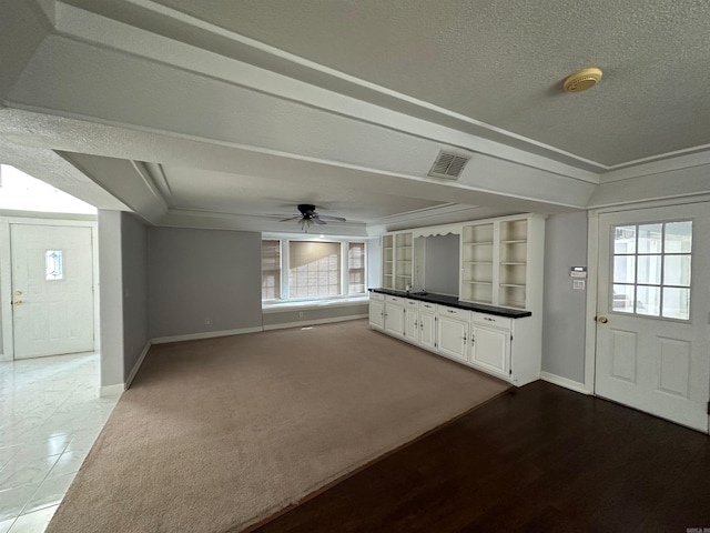 unfurnished living room with built in features, a textured ceiling, light carpet, ceiling fan, and crown molding