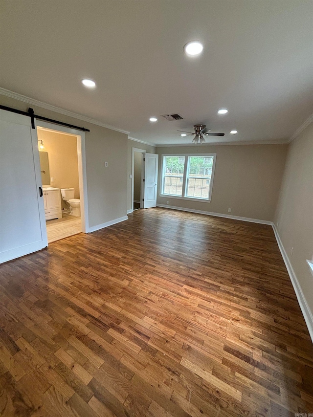 unfurnished living room featuring a barn door, hardwood / wood-style flooring, ceiling fan, and crown molding