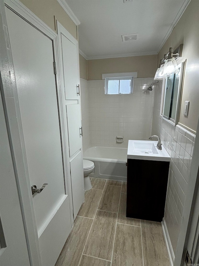 full bathroom with tile walls, crown molding, vanity, tiled shower / bath combo, and toilet