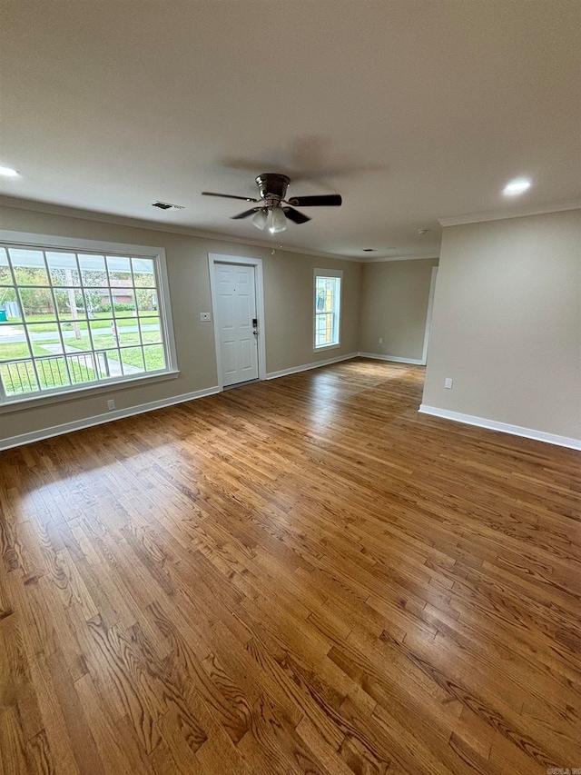 empty room featuring ceiling fan, hardwood / wood-style floors, a healthy amount of sunlight, and crown molding