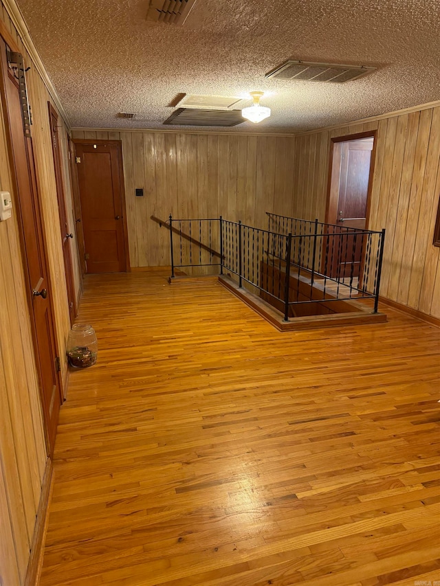 corridor with light hardwood / wood-style flooring, wooden walls, and a textured ceiling