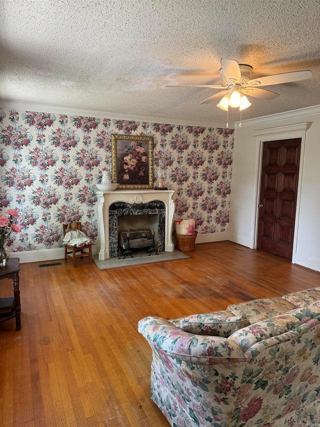 living room with ceiling fan, hardwood / wood-style floors, a high end fireplace, ornamental molding, and a textured ceiling