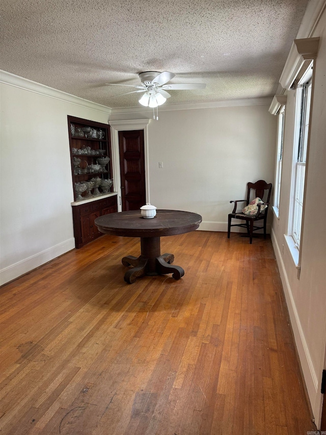 unfurnished dining area with wood-type flooring, a textured ceiling, crown molding, and ceiling fan